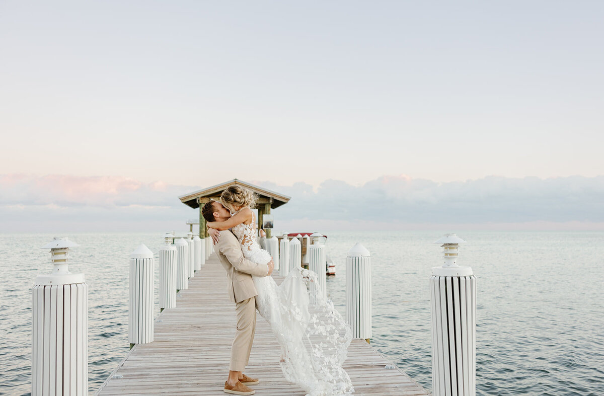 Hunter lifts Ashley up as he kisses her, with the ocean and the dock framing the perfect shot.