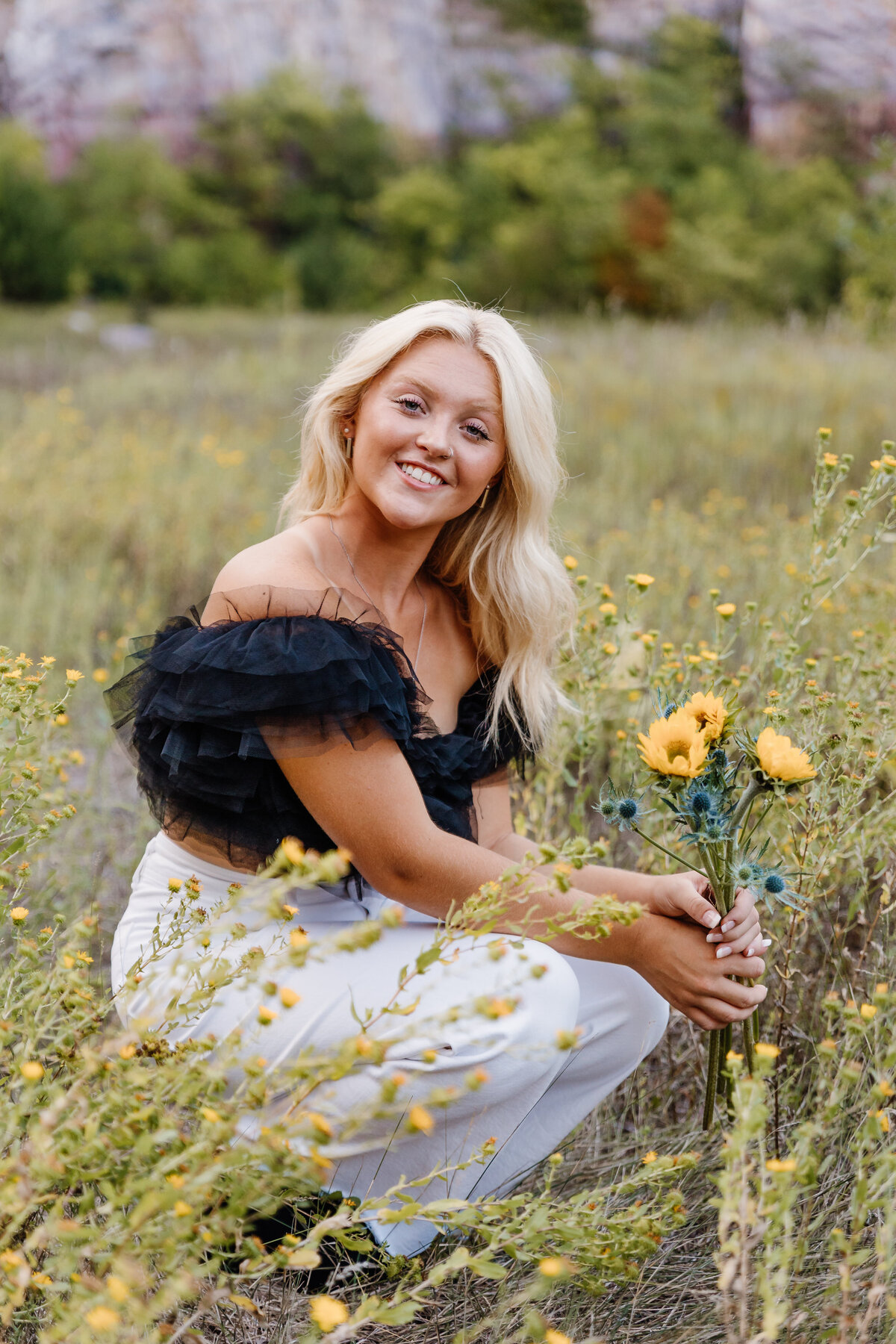 A girl crouched down in a field holding flowers