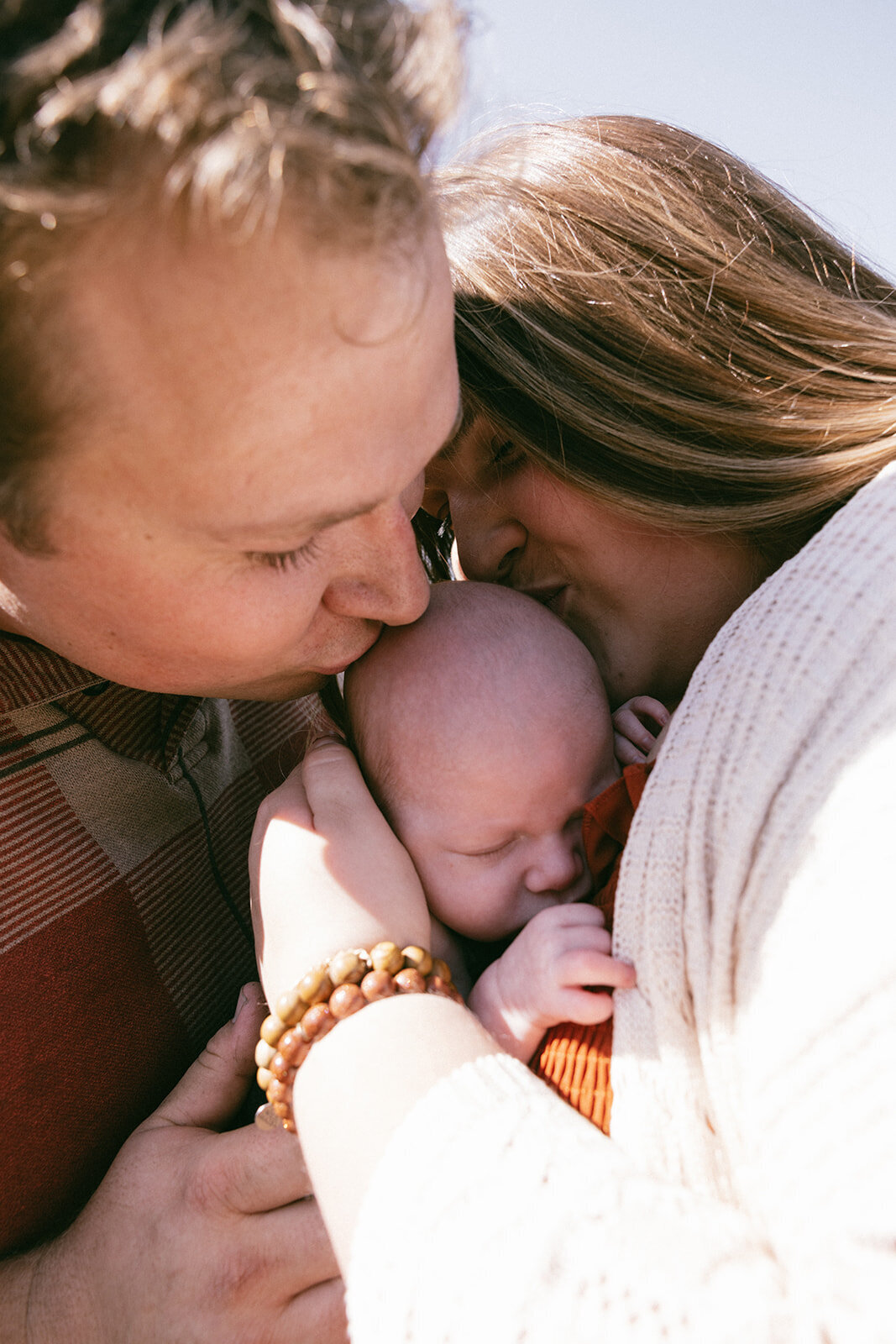Mother and father kiss infants head while doused in the San Diego sunlight. 