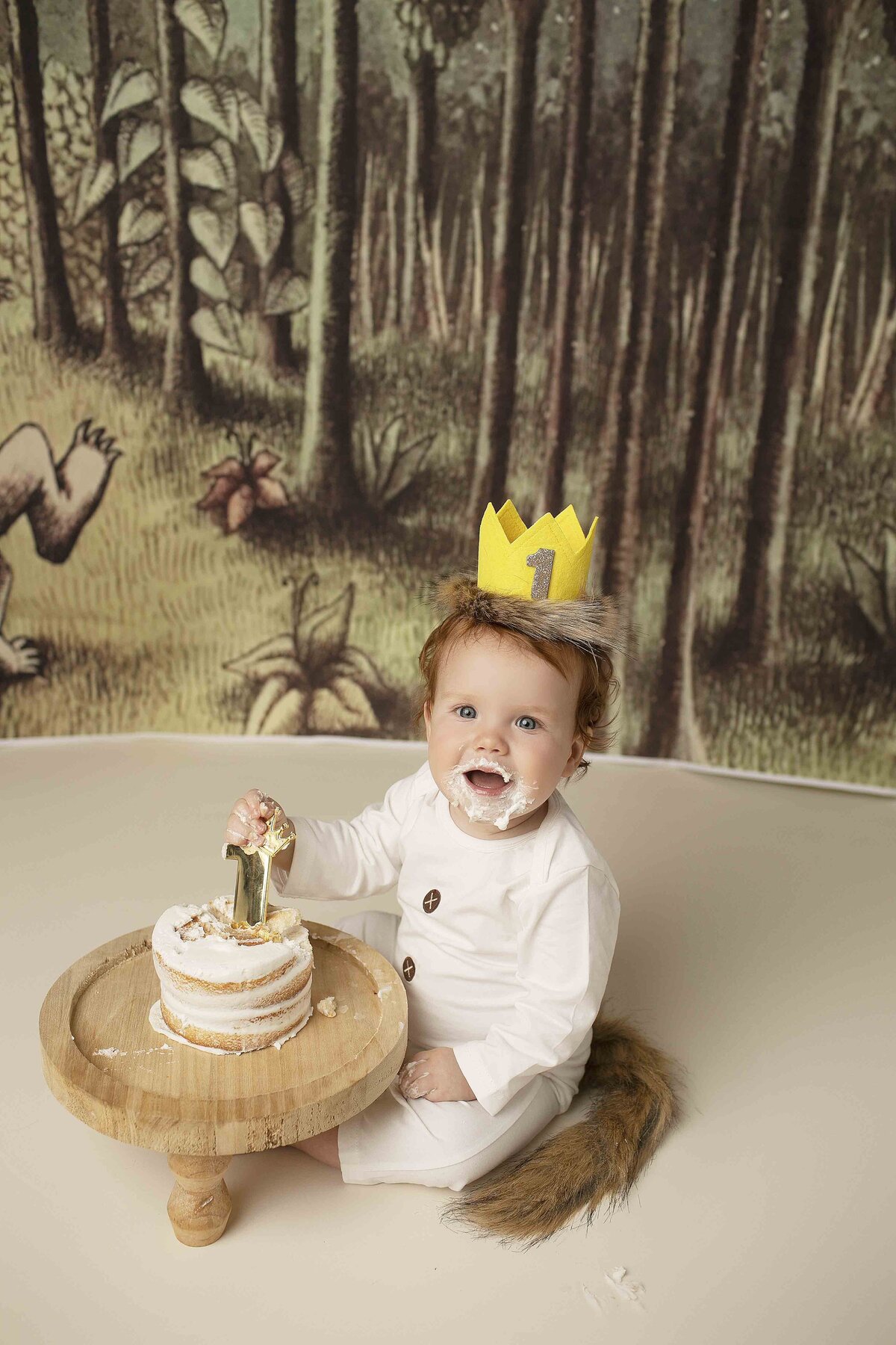 Redhead birthday boy in a playful Where the Wild Things Are outfit, happily digging into his cake during the cake smash