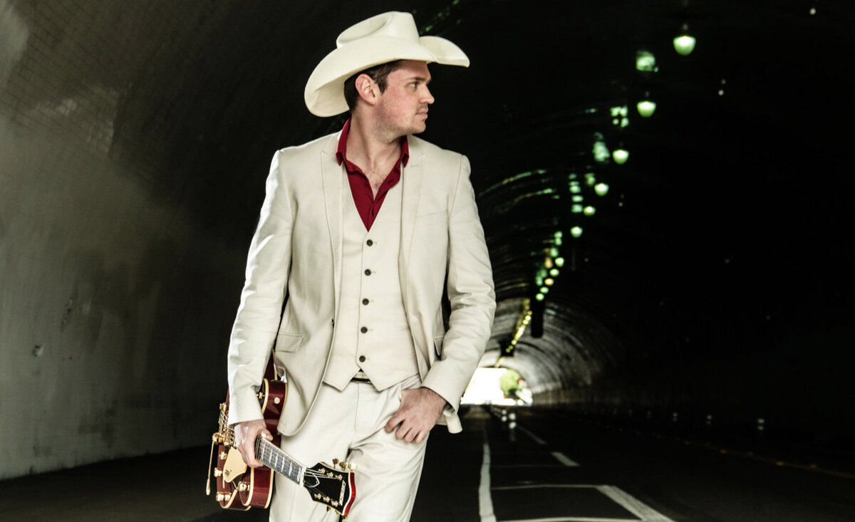 Country music photo Ben Klick walking through tunnel wearing white suit white cowboy hat carrying white guitar