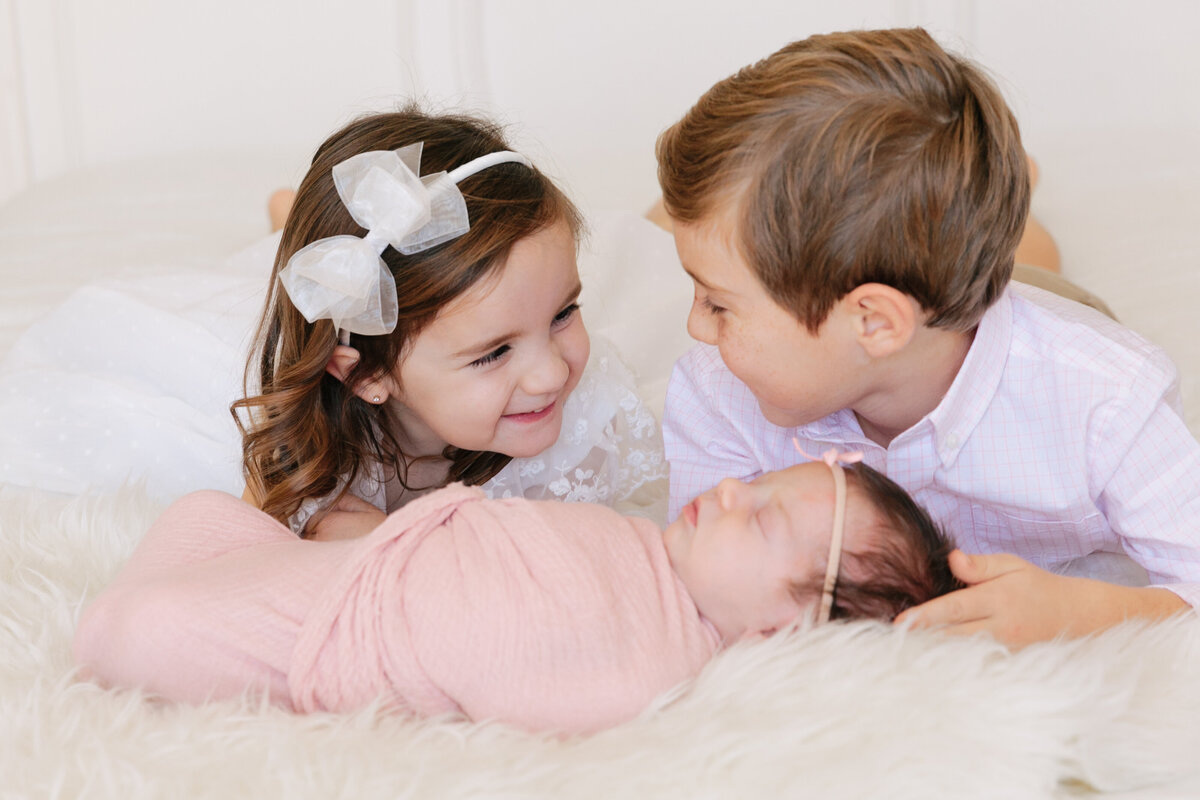 Two siblings laying on a bed with a newborn baby