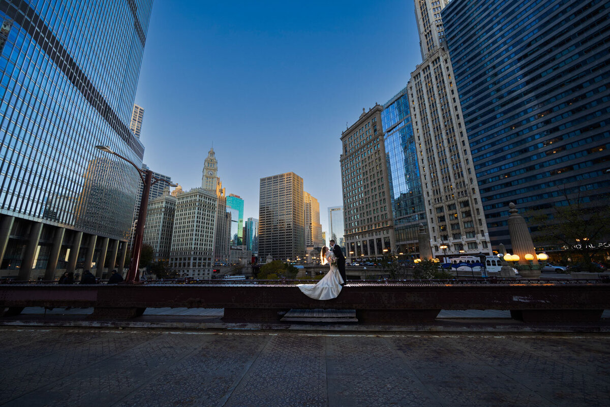 A bride and groom are posing for a picture in front of a city skyline.