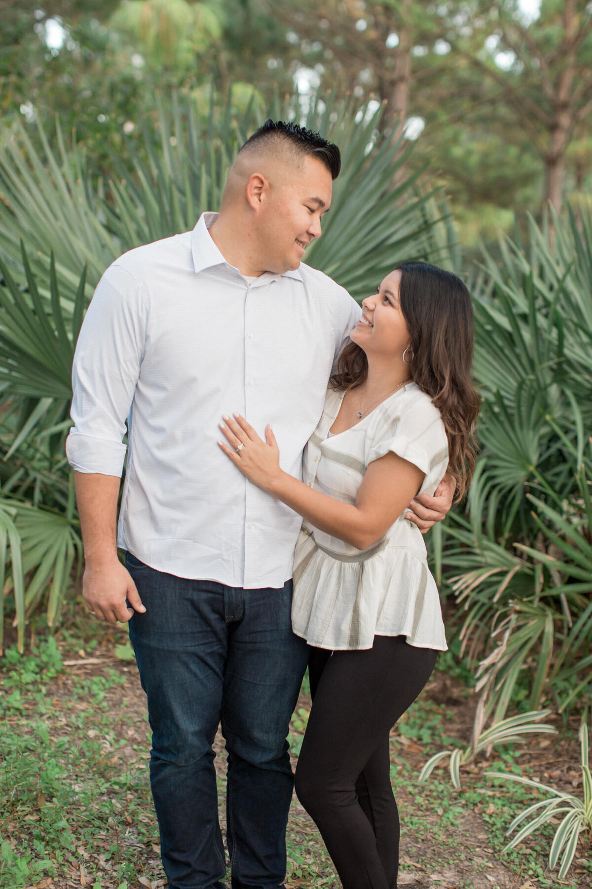 A latino couple stand in front of tropical plants during their engagement session