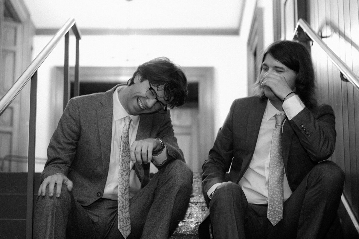 Groom and his best man share a laugh in black and white while waiting a wedding ceremony. 