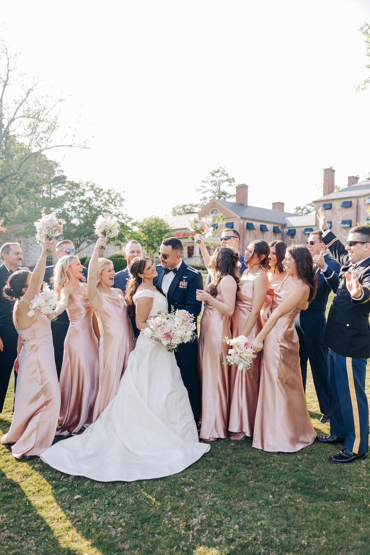 A wedding celebration outdoors with a joyful bridal party surrounding the bride and groom.