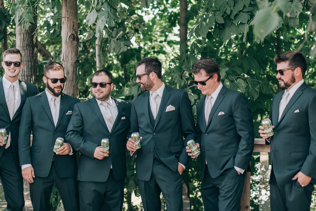 Groom and groomsmen wearing green suits having a drink before the wedding ceremony