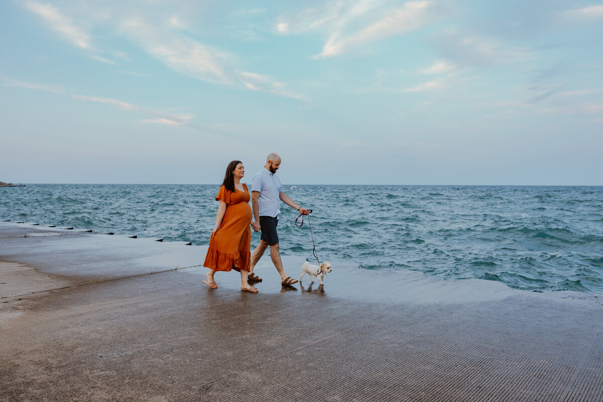 Husband and wife walking lake front during maternity session in Chicago, IL