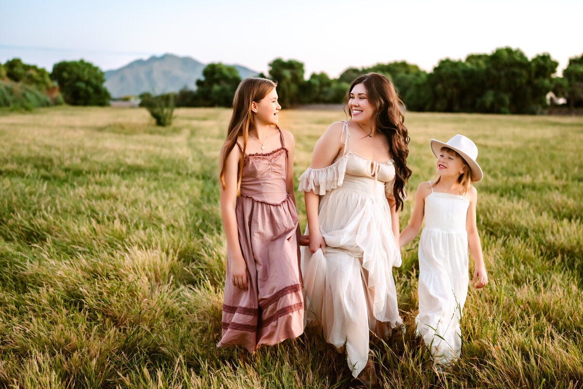 Mom holding daughters hands in green field in Arizona