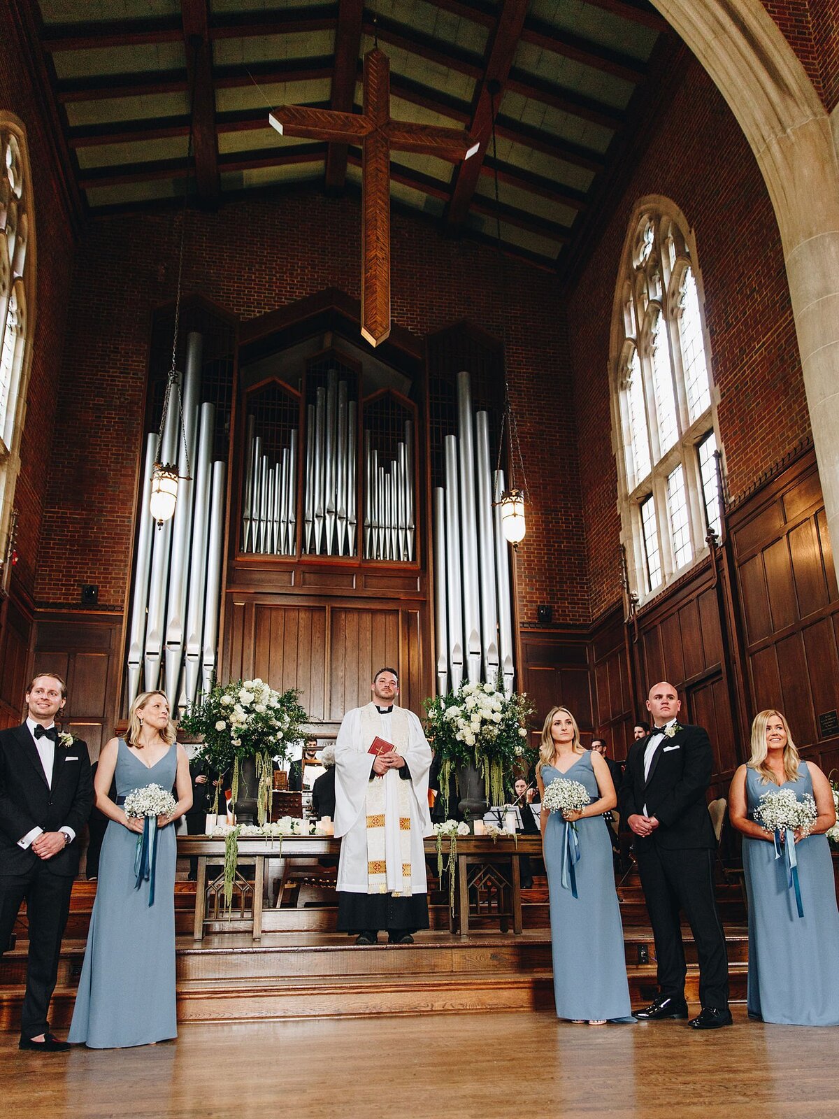 The altar with a floor length pipe organ  at Scarritt Bennett's Wightman Chapel. The bridal party wearing black tuxedos, dusty blue dresses and white bouquets stand waiting for the couple.