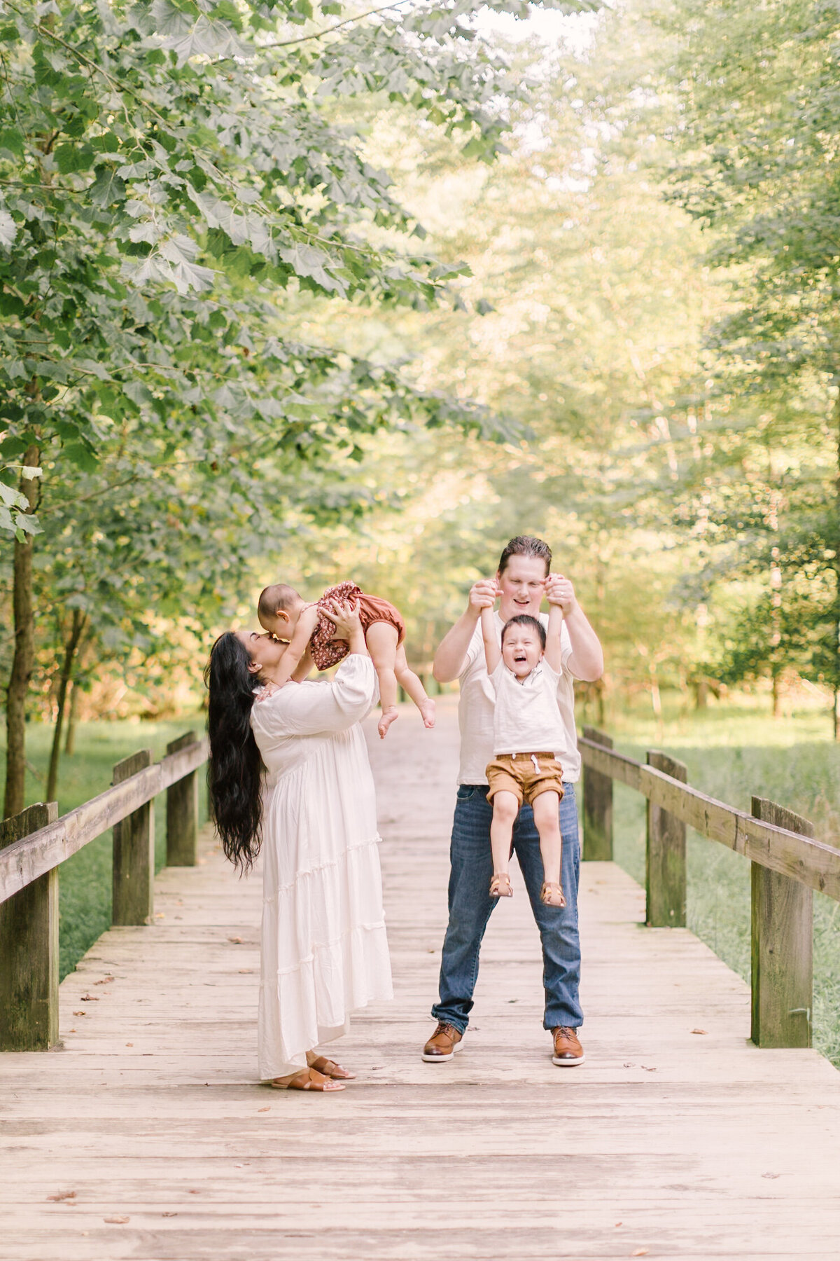 A family walking along a wooden bridge surrounded by summer greenery — Portrait photos in Raleigh.