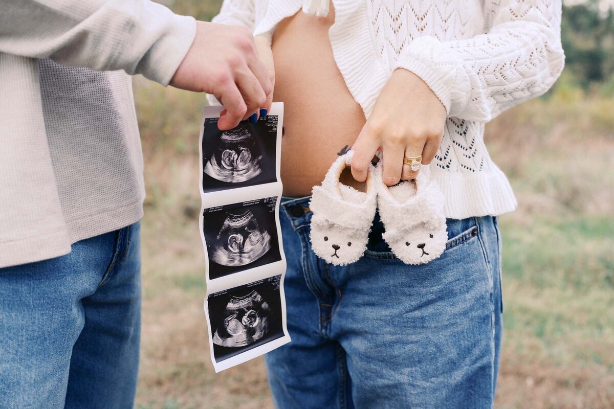 pregnant mom holds ultrasound and baby shoes for maternity pictures at seven islands state birding park in kodak tennessee