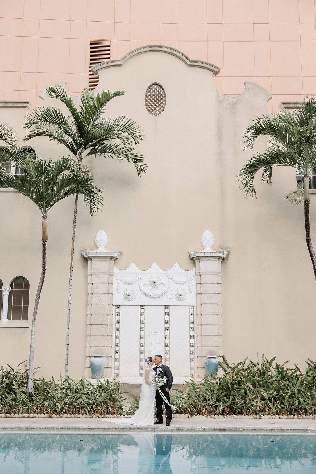 Bride and groom standing in front of Cafe Julia iconic pool with palm trees surrounding them