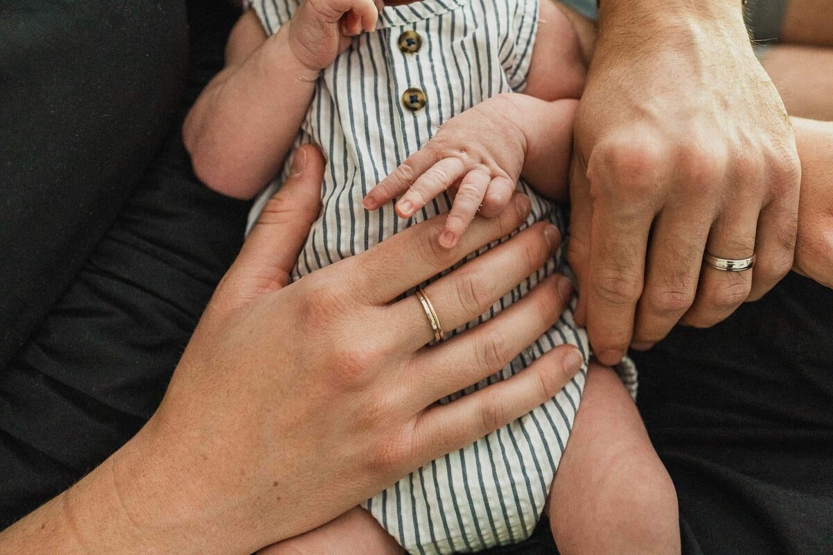 A close-up shot of parents’ hands gently cradling their newborn, capturing the bond and love of family during in-home lifestyle photography session.