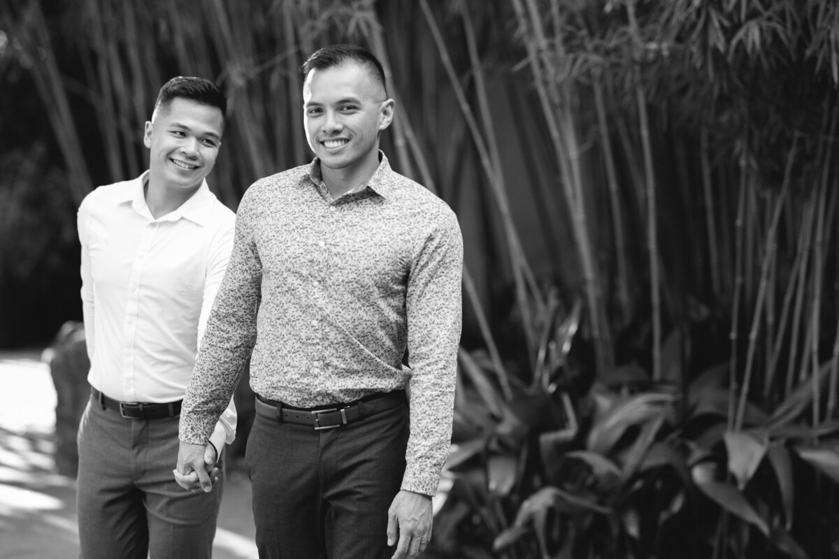 Gay couple walking at Dallas World Aquarium in black and white during their engagement session, one glancing at the camera while the other looks at his fiancé.
