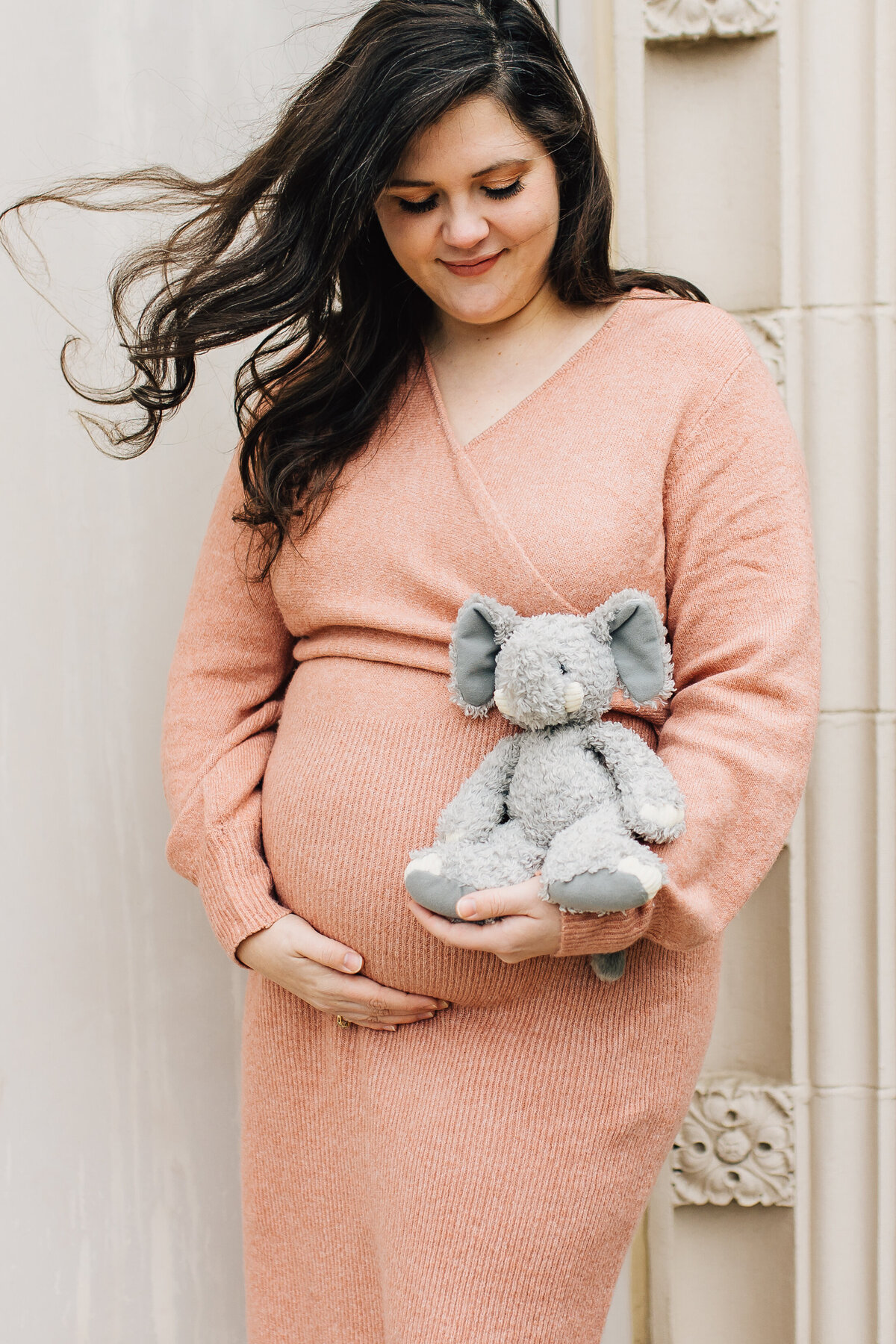 Pregnant woman smiles while holding her baby and a stuffed animal