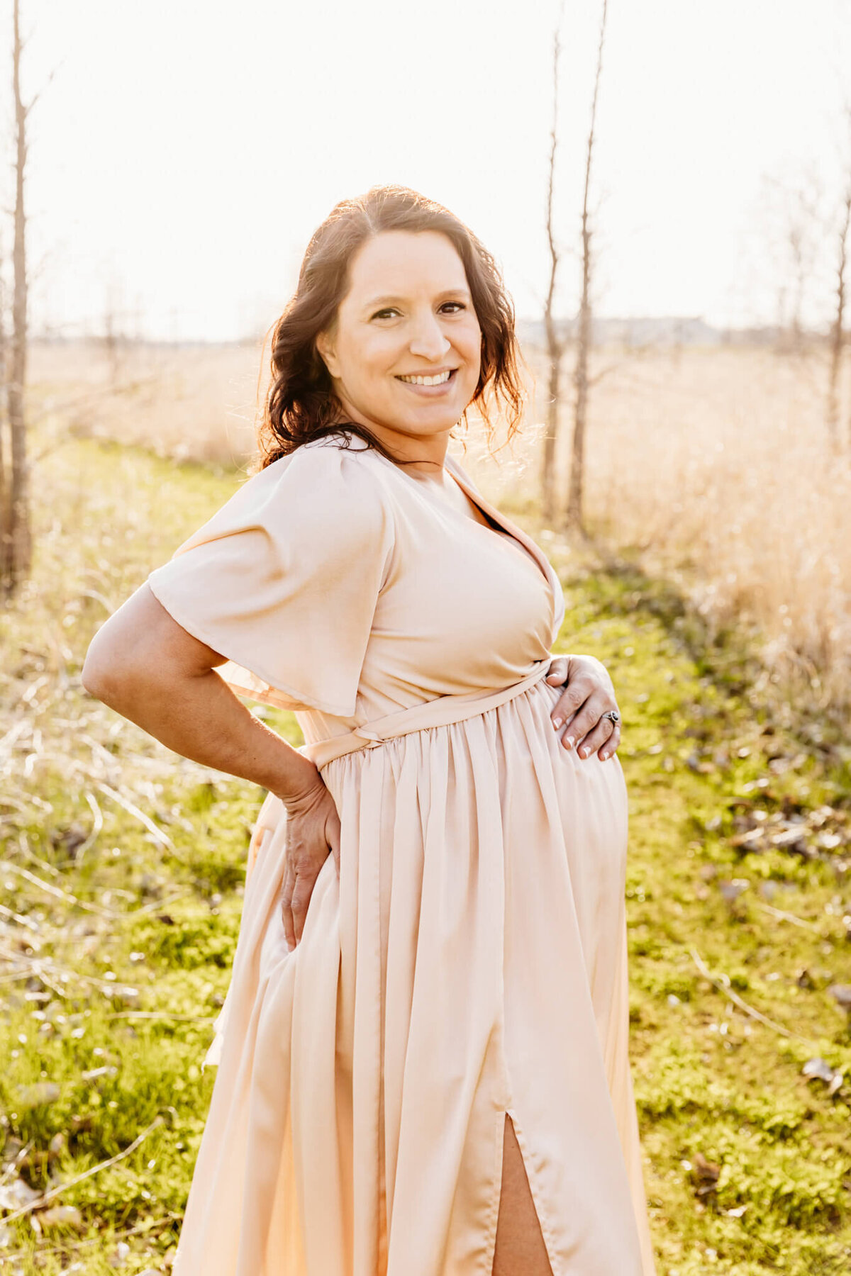 pregnant woman showing off her baby bump in a golden field by Ashley Kalbus Photography
