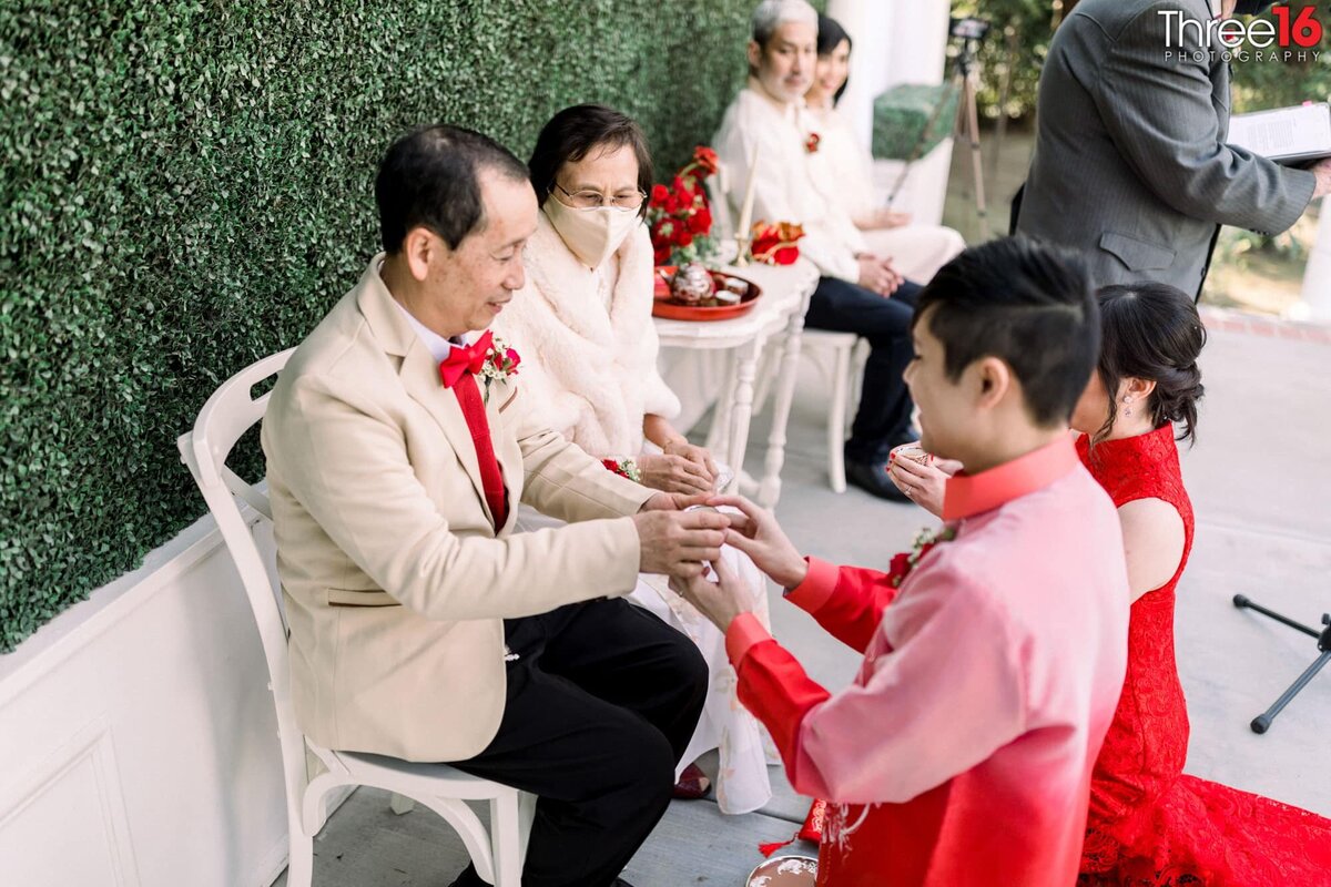 Bride and Groom kneel as they present tea to her parents