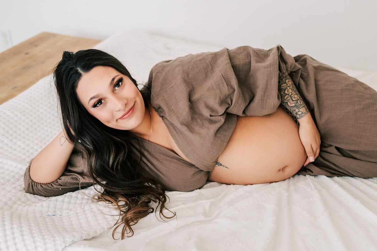 pregnant mom laying on bed holding baby bump during Springfield MO photography session