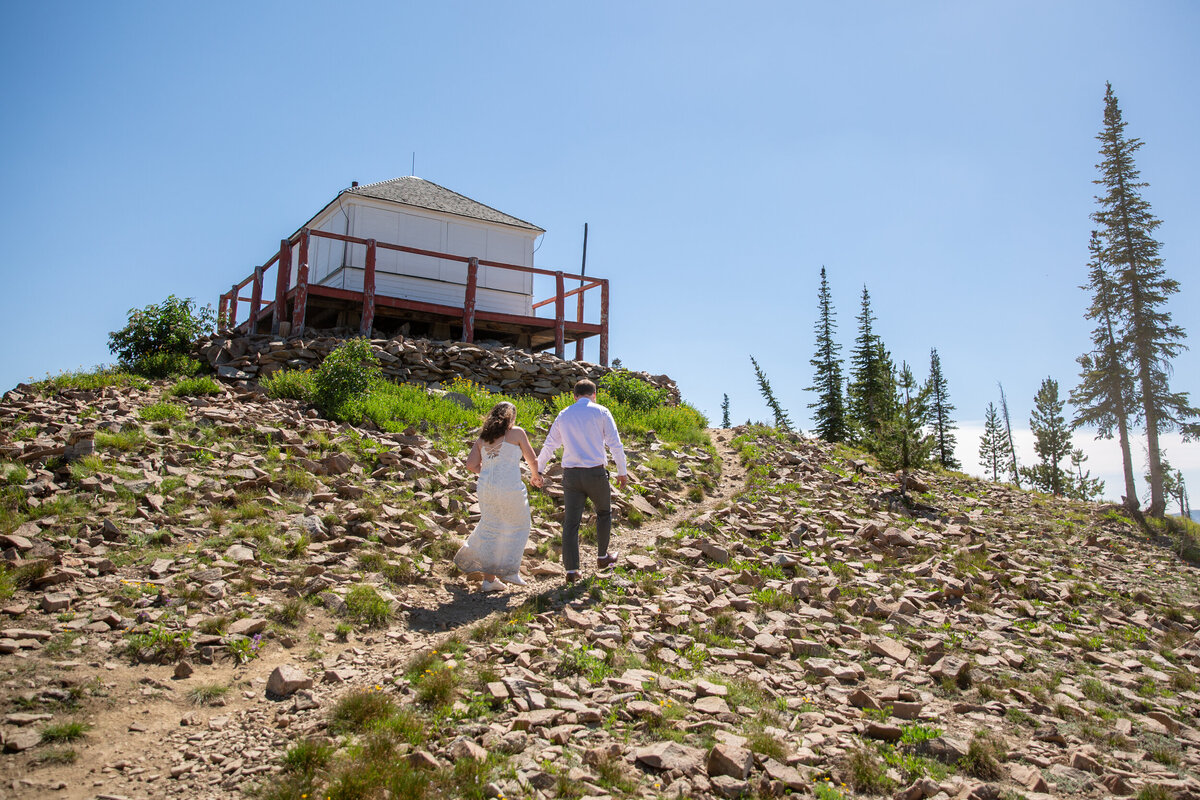A bride and groom walk up a hill to a fire lookout in Idaho on their elopement day.