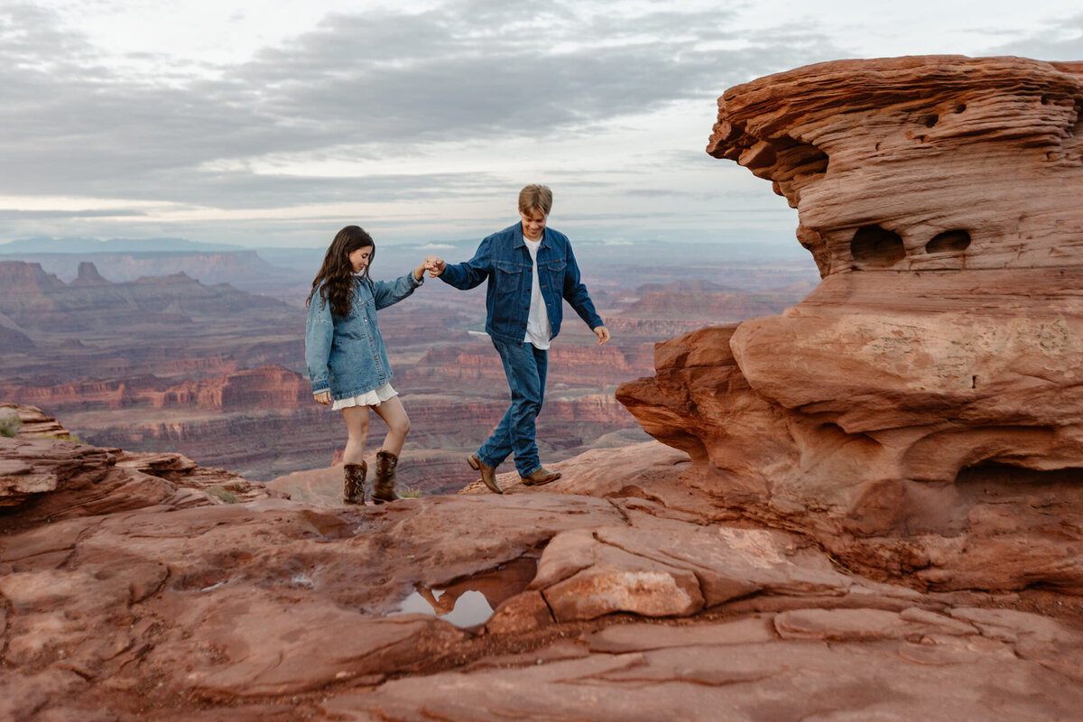 A couple holding hands, and  in all denim,  walk on the red rocks of Utah