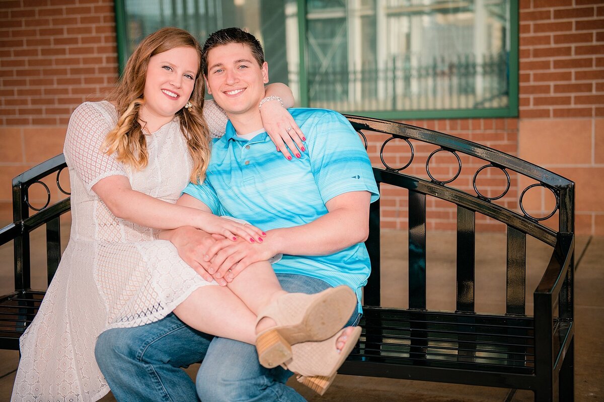 Bride-to-be sits on fiancé's lap on bench at Station Square in Pittsburgh, PA