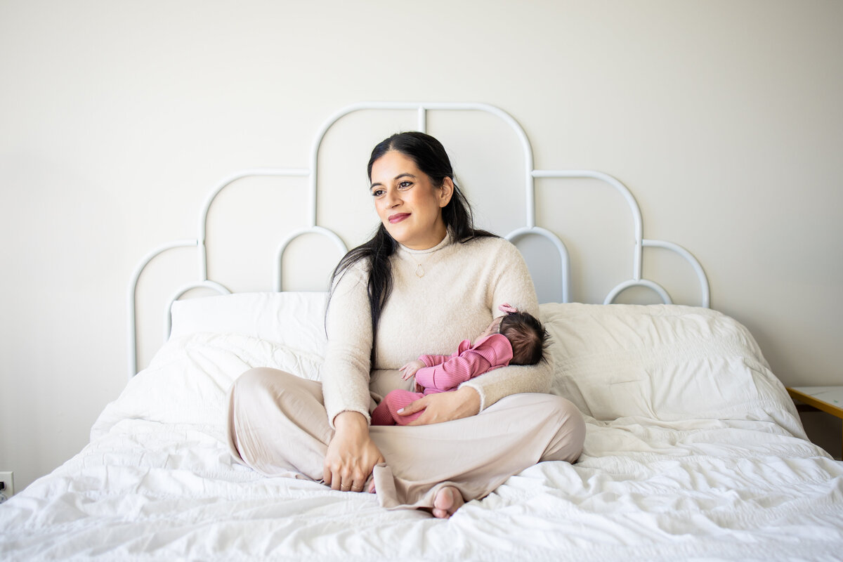 Mom sitting on white bed cradling baby girl in her arms