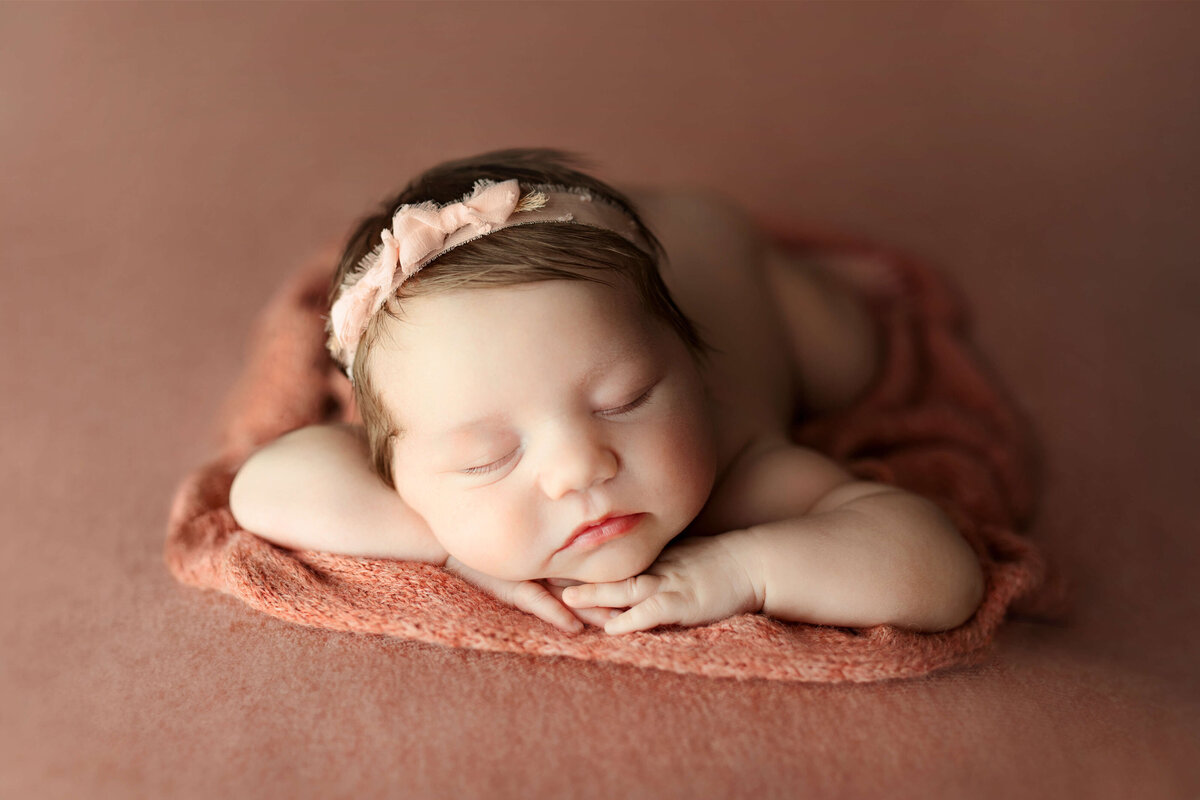 newborn baby laying on a pink backdrop with a pink bow headband