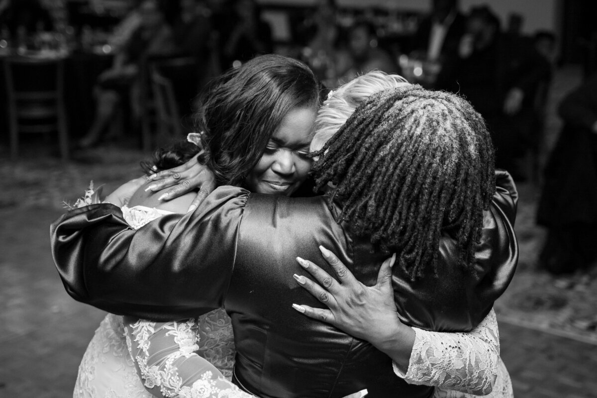 Bride emotionally hugs her mother and mother-in-law during their first dance together at her wedding at the Wigwam Event Center.