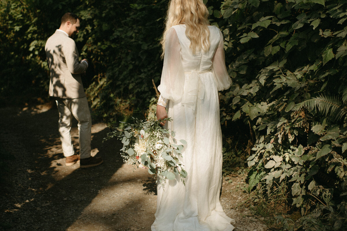 bride holding bouquet and walking towards groom in ivy covered pathway