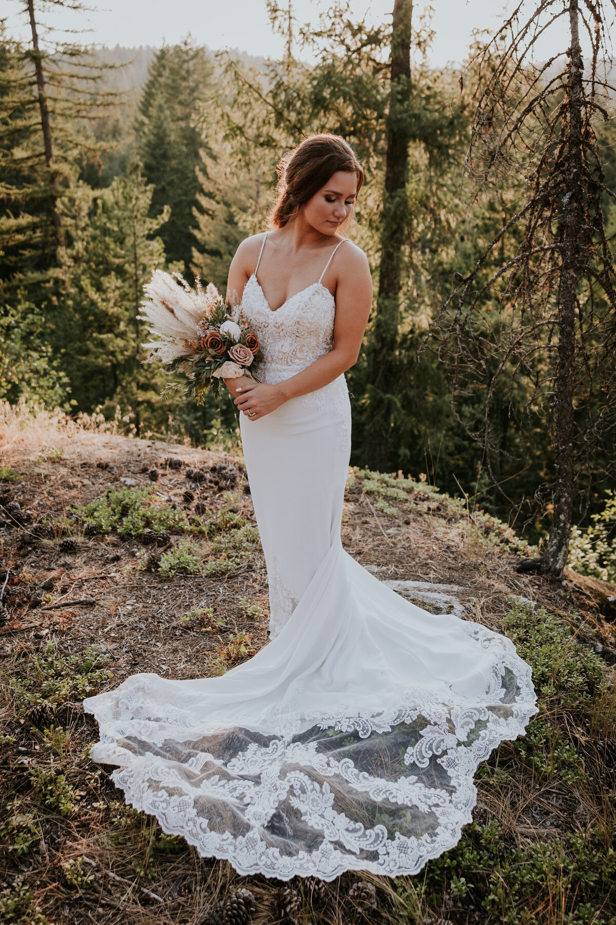 Bride stands with bouquet while looking down at train of her gown.