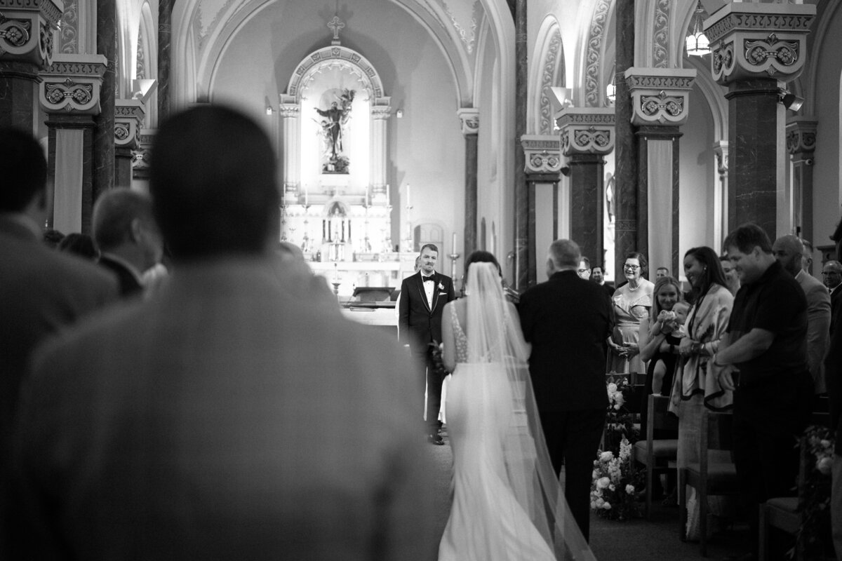 Bride walks down aisle while groom shows emotion