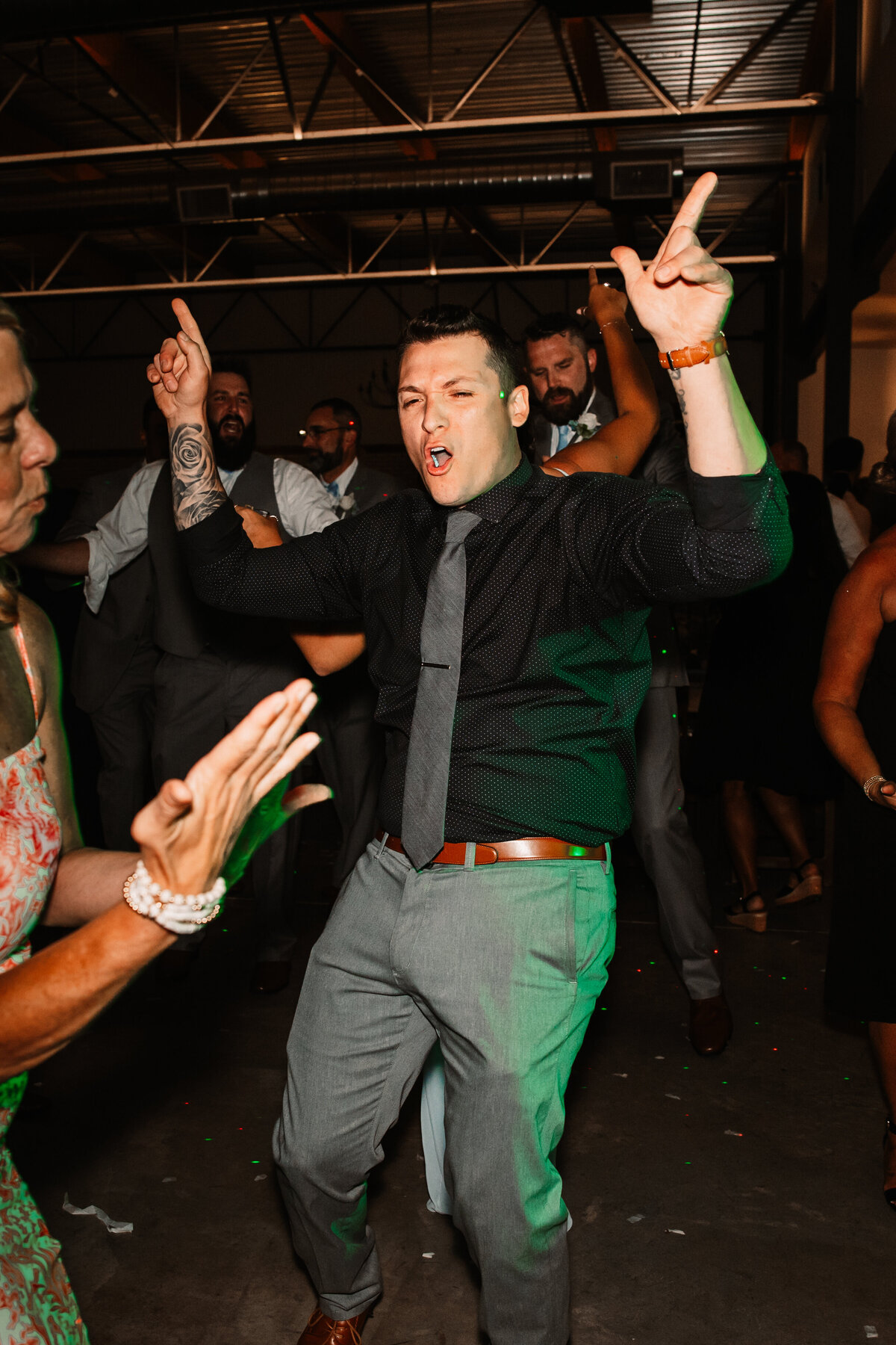 A man in a black shirt and grey pants dances on a crowded dance floor at a reception