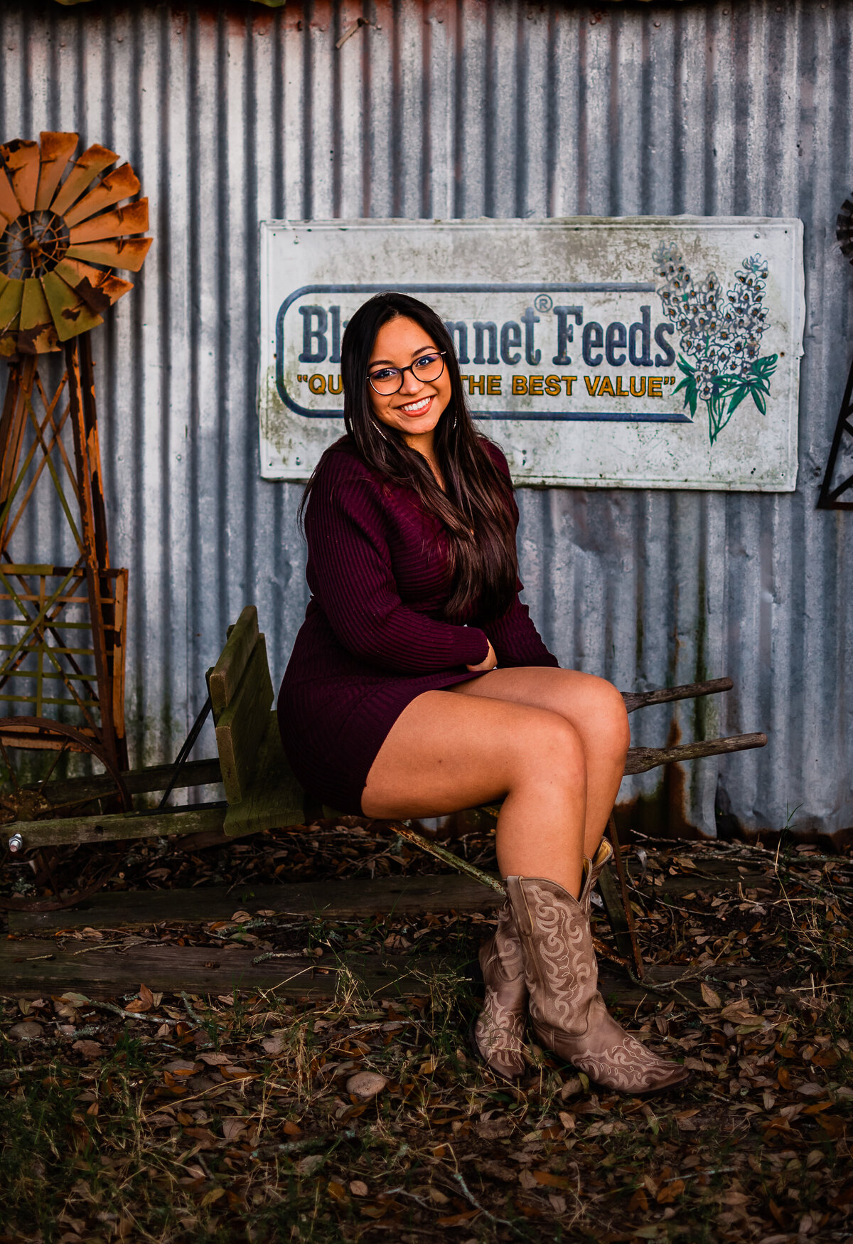 A Clear Creek High School graduate sits in front of a tin building on an antique wheel barrow.