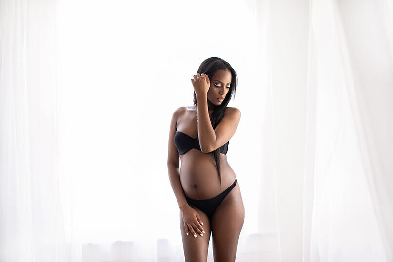 Pregnant black woman posing in white studio wearing black bikini