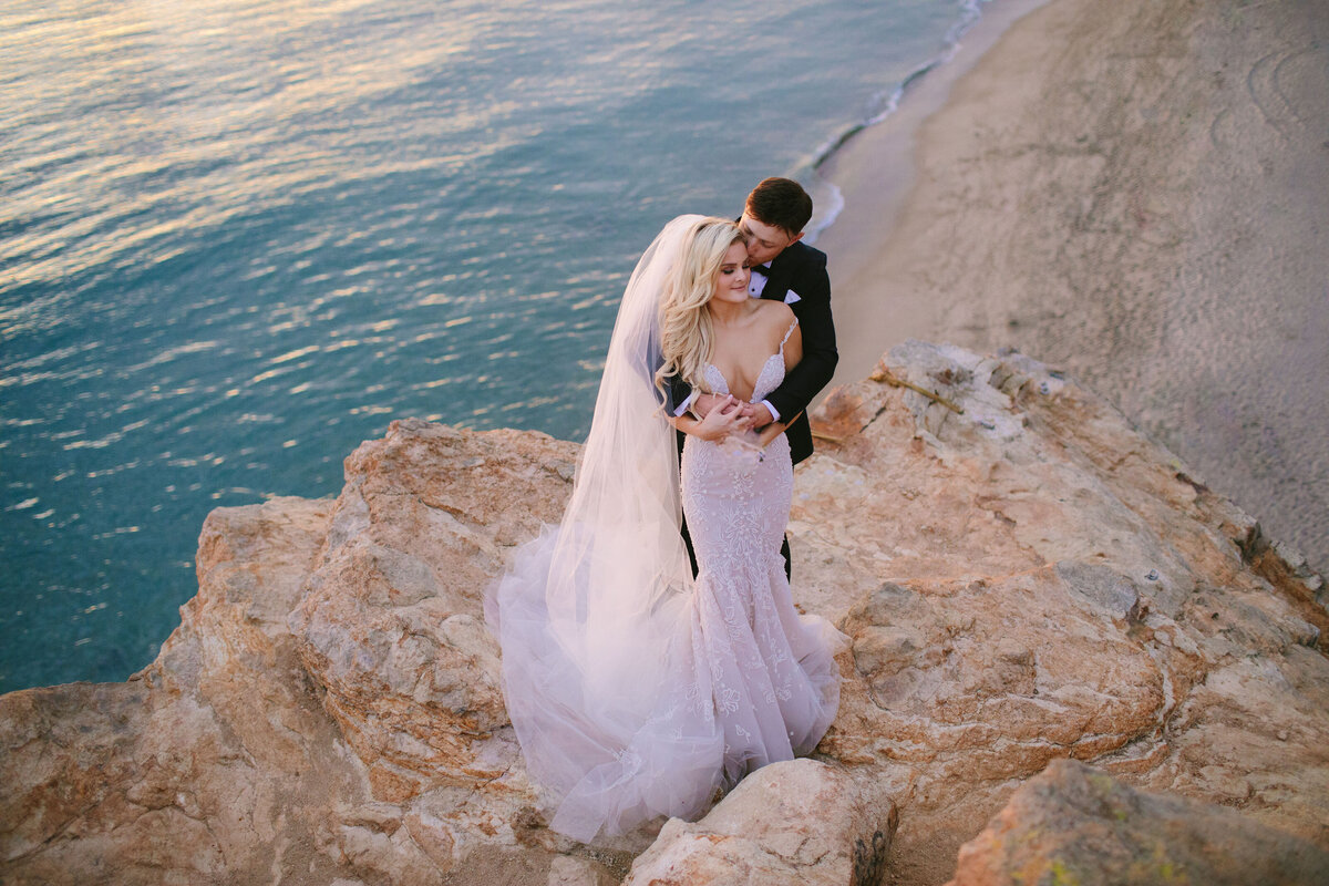An eloping couple embraces on the cliffside overlooking the ocean at a beach in Malibu, California.