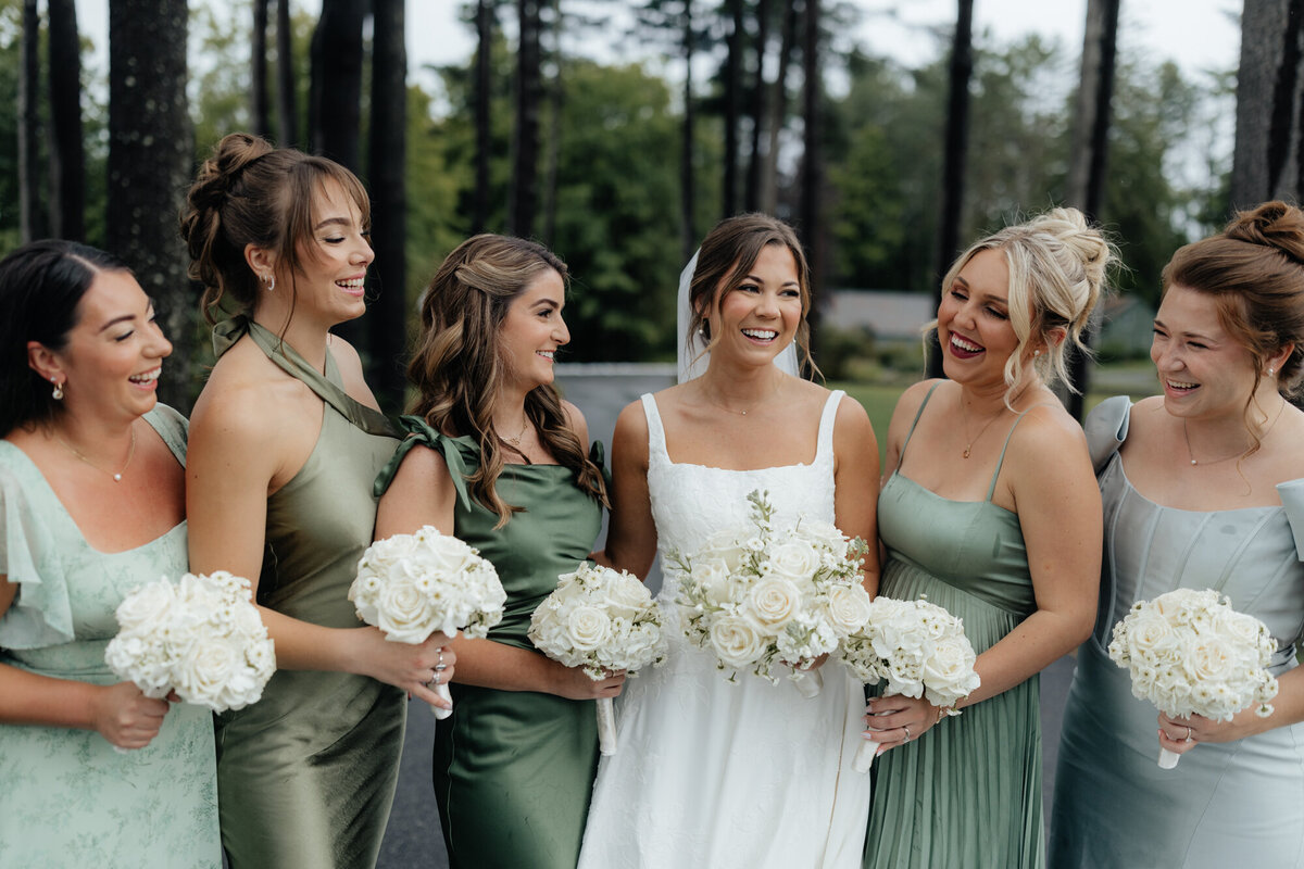 Bridesmaids in sage green dresses holding white bouquets beside bride