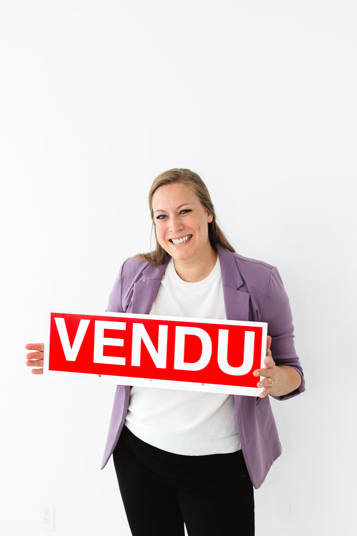 Real Estate Agent, Sophia, holding up a French sign that says SOLD.