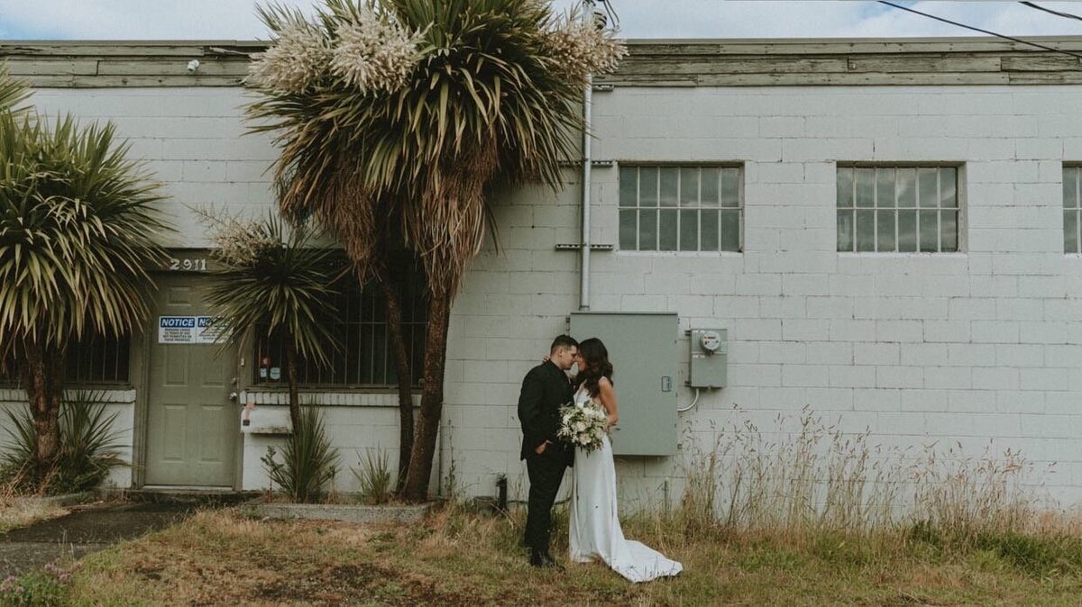 Bride and groom stand outside of an old building with palm trees