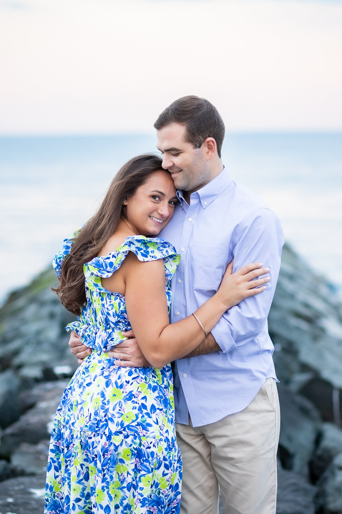 julia and pat embrace atop the rocks at their Fairfield beach engagement session