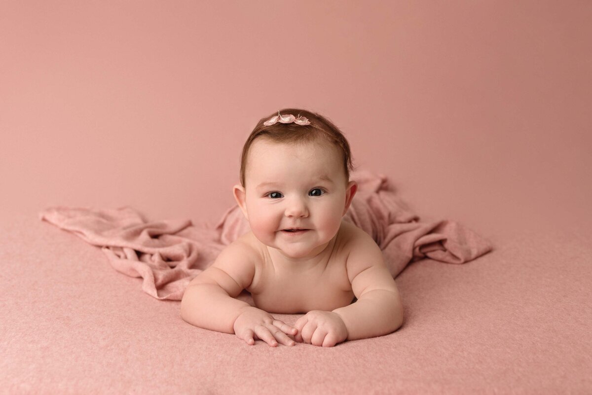 Three month old baby girl laying on tummy on pink blanket with matching headband and swaddle