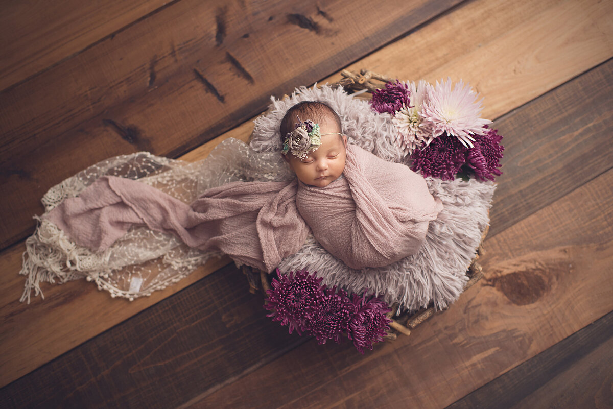 a newborn girl with pink and purple fur on wood backdrop shot from above