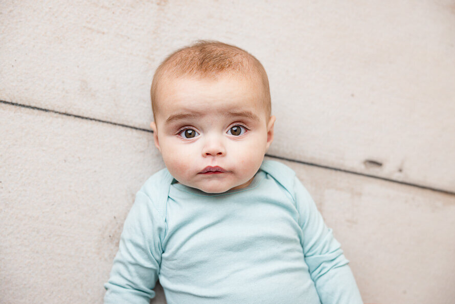Baby boy on back in blue onesie stares right into camera.
