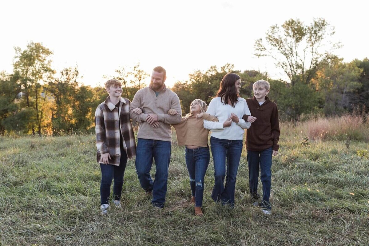 A family of five stands together in an open field, enjoying the golden glow of the setting sun.
