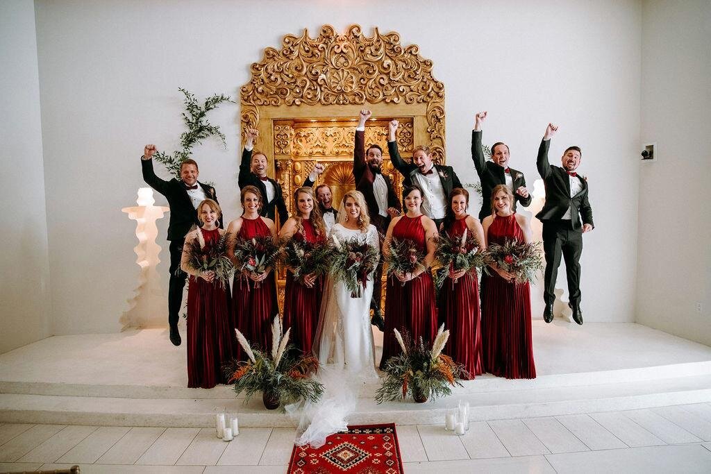 Bridal party celebrates with the bride and groom with bridesmaids in burgundy dresses.