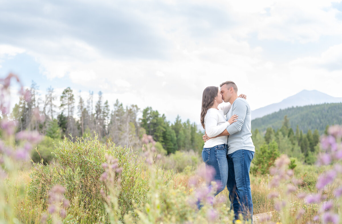 couple going in for a romantic kiss among the purple wildflowers in rocky mountain national park in Colorado