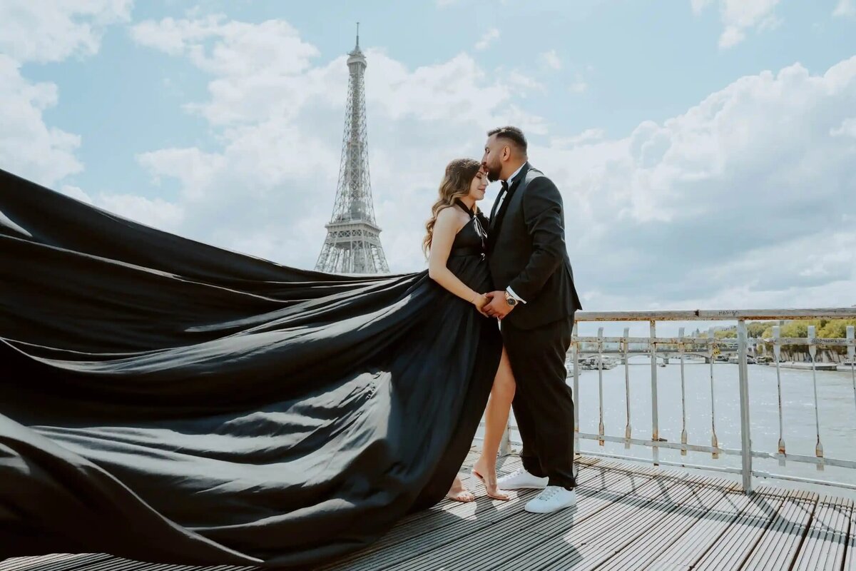 a couple having a photoshoot in front of the eiffel tower with a black flying dress