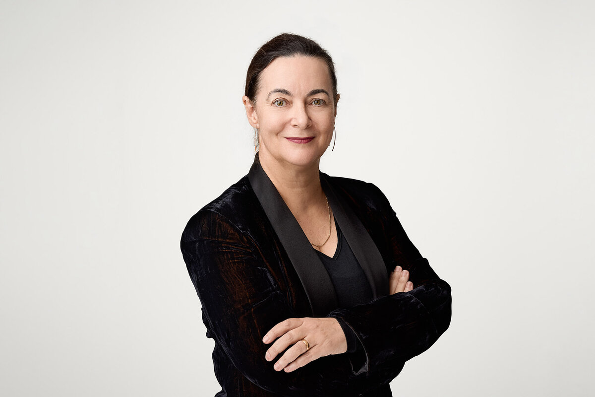 Woman arms folded in a black velvet jacket against white background. She has a soft smile.