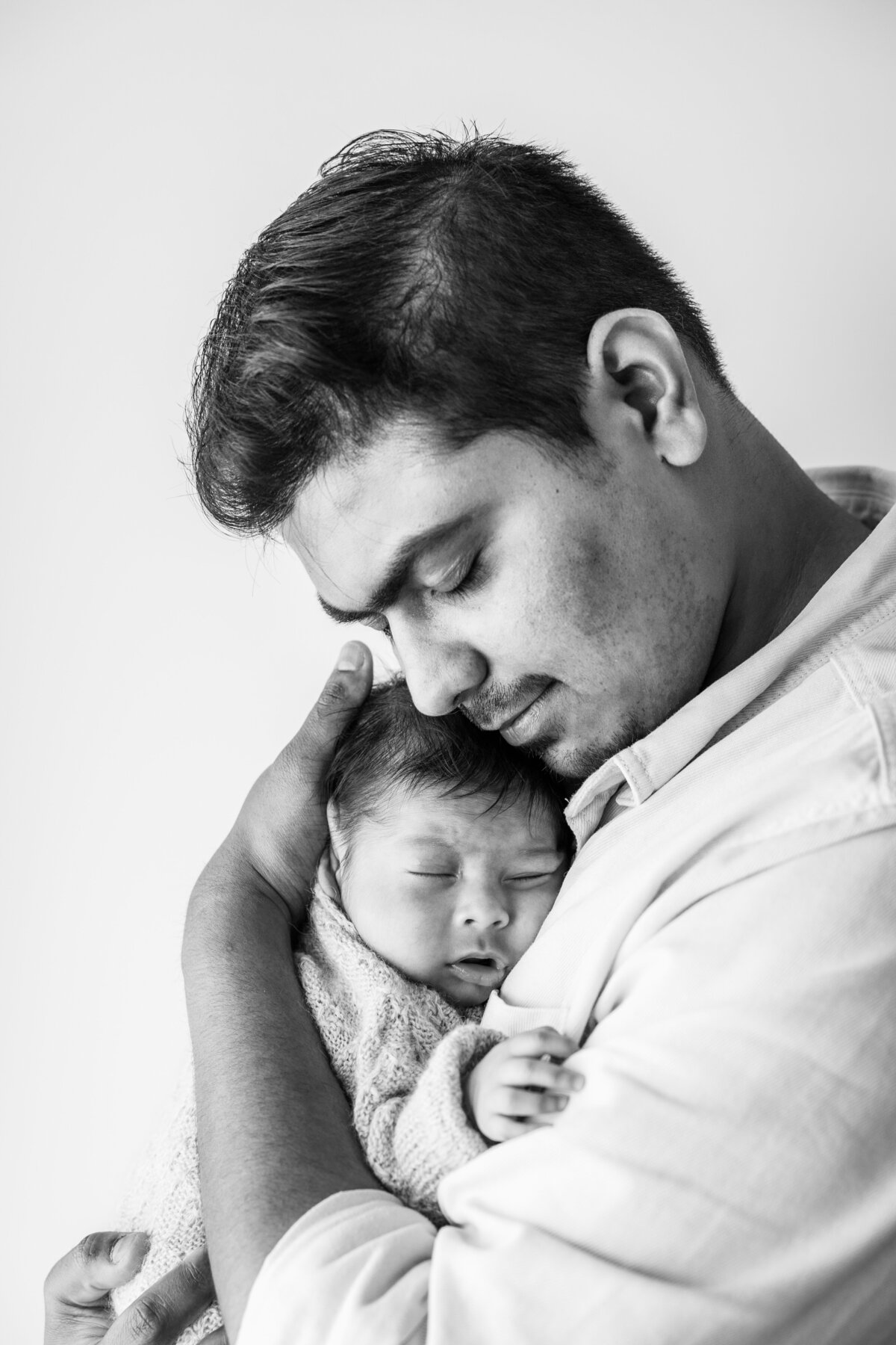 Black and white image of father holding newborn baby close to his chest