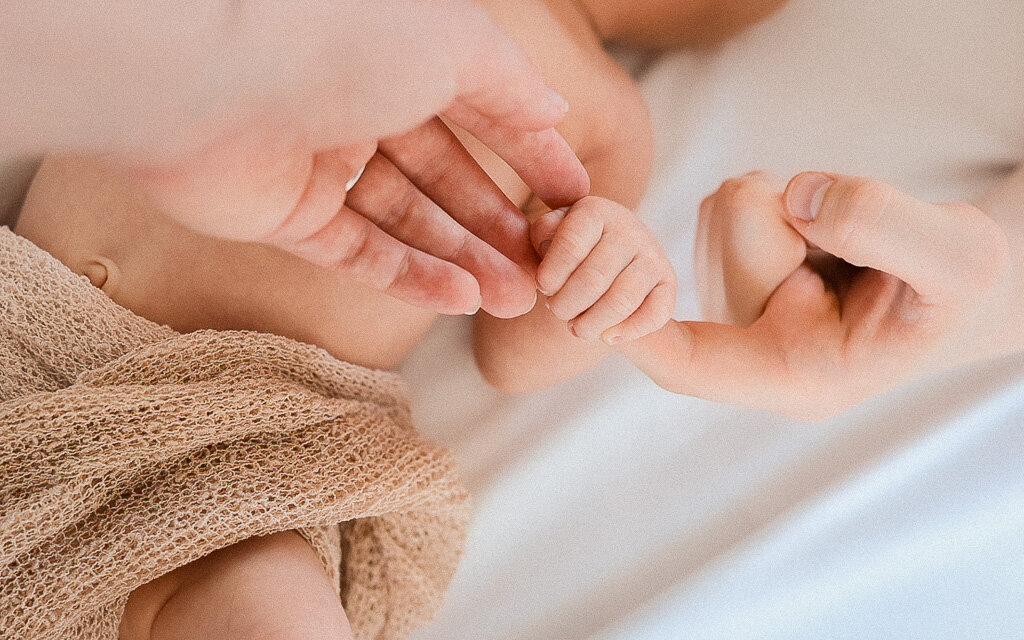 Close-up of tiny baby hands holding mothers and fathers hand capturing delicate newborn details in soft natural light. Lifestyle photography by Nostalgia - Sophie Louise